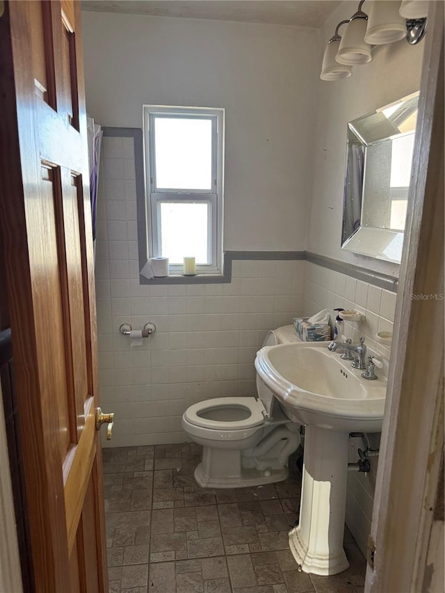 bathroom with wainscoting, toilet, and tile walls