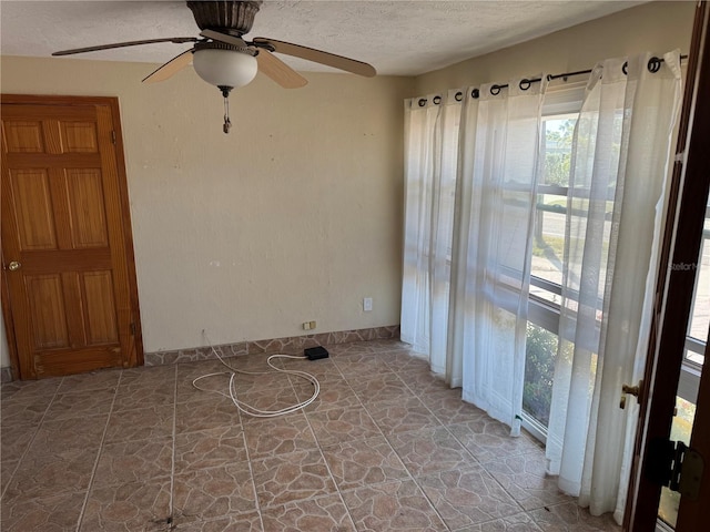 unfurnished room with a textured ceiling, stone finish flooring, a wealth of natural light, and baseboards