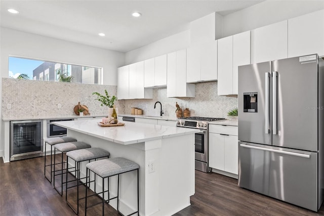 kitchen featuring a kitchen island, appliances with stainless steel finishes, a kitchen breakfast bar, white cabinetry, and a sink