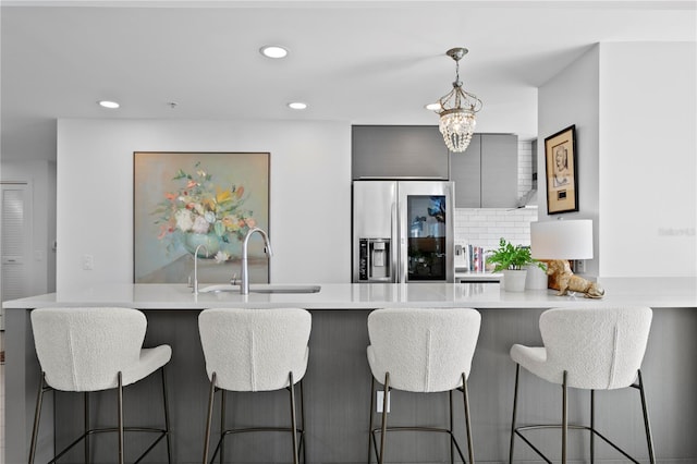 kitchen featuring a kitchen bar, sink, decorative light fixtures, stainless steel fridge, and kitchen peninsula