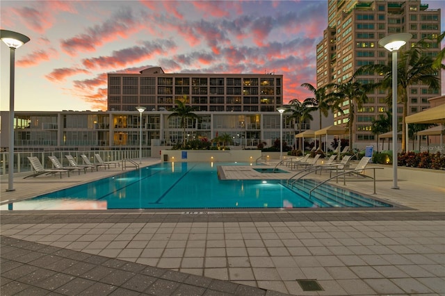 pool at dusk featuring a jacuzzi and a patio area