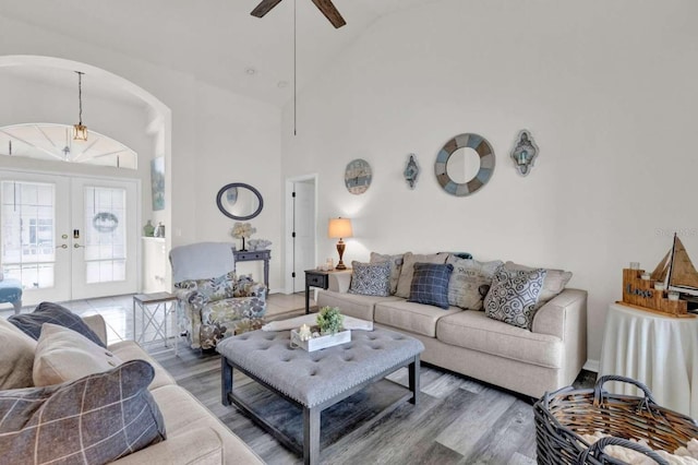 living room with arched walkways, high vaulted ceiling, ceiling fan, wood finished floors, and french doors