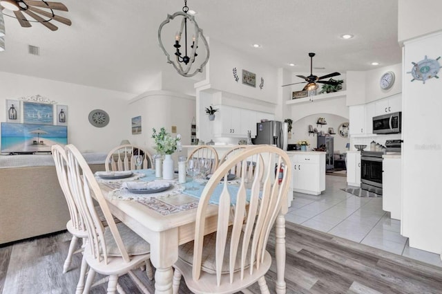 dining area featuring visible vents, arched walkways, light wood-style floors, high vaulted ceiling, and ceiling fan with notable chandelier