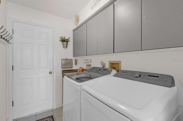 laundry room featuring a textured ceiling, separate washer and dryer, light tile patterned floors, and cabinet space