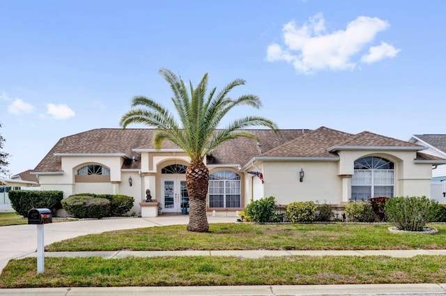 mediterranean / spanish home featuring french doors, driveway, a front lawn, and stucco siding