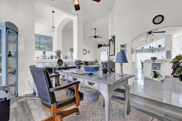 dining room with a towering ceiling, arched walkways, wood finished floors, and a ceiling fan