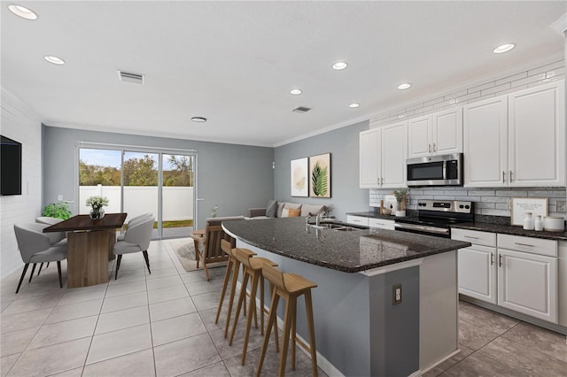 kitchen featuring sink, stainless steel appliances, white cabinets, a center island with sink, and dark stone counters