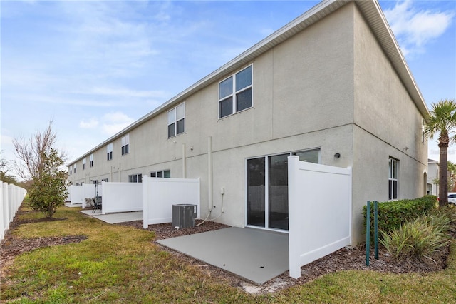 rear view of house with central AC, a patio area, and a lawn