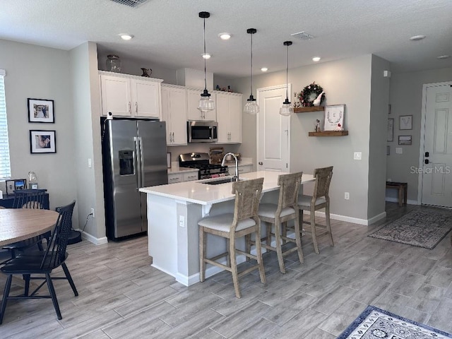 kitchen with stainless steel appliances, hanging light fixtures, a kitchen island with sink, and white cabinets