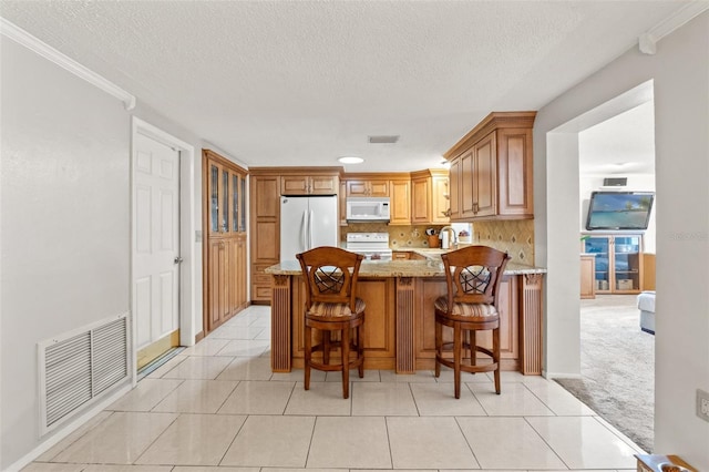 kitchen featuring white appliances, a breakfast bar, light stone countertops, a textured ceiling, and kitchen peninsula