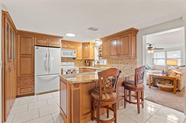 kitchen featuring light stone counters, white appliances, a kitchen breakfast bar, and light tile patterned flooring