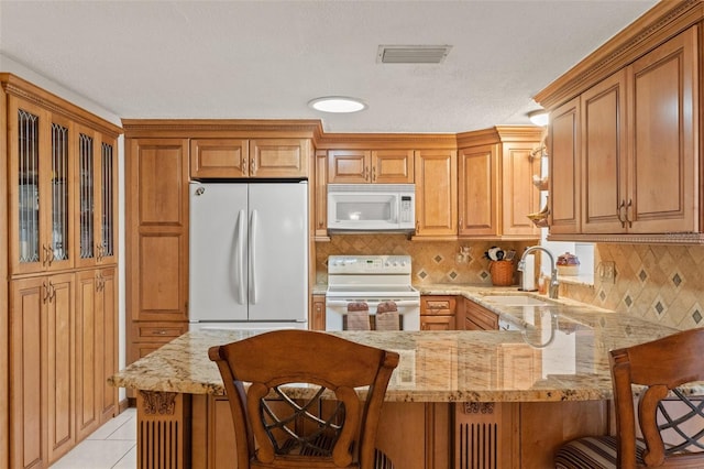 kitchen featuring sink, white appliances, a breakfast bar area, and kitchen peninsula