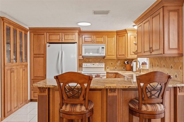 kitchen with a kitchen bar, sink, tasteful backsplash, light tile patterned floors, and white appliances