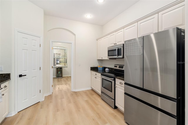 kitchen with dark stone countertops, light wood-type flooring, white cabinets, and appliances with stainless steel finishes