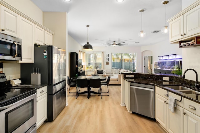 kitchen with appliances with stainless steel finishes, sink, hanging light fixtures, and dark stone counters