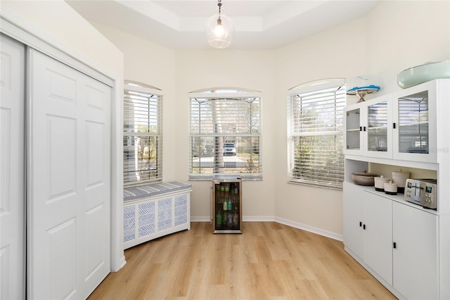 bedroom featuring beverage cooler, a raised ceiling, light hardwood / wood-style floors, and multiple windows