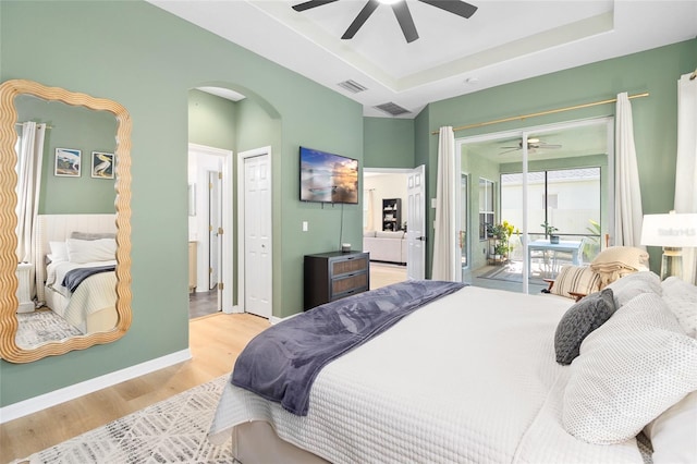 bedroom with ensuite bath, access to exterior, a raised ceiling, and light hardwood / wood-style floors