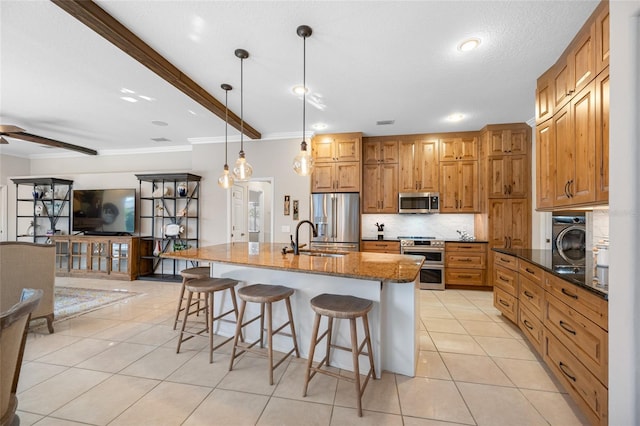 kitchen with a kitchen island with sink, hanging light fixtures, stainless steel appliances, dark stone counters, and light tile patterned flooring