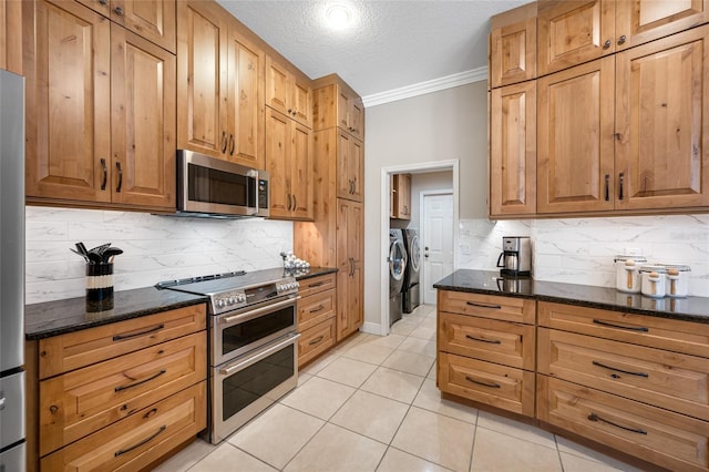 kitchen featuring ornamental molding, stainless steel appliances, dark stone countertops, and separate washer and dryer