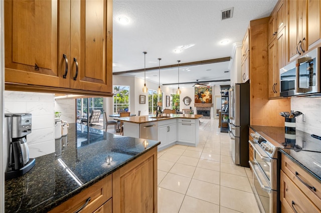 kitchen with backsplash, light tile patterned floors, dark stone counters, appliances with stainless steel finishes, and pendant lighting