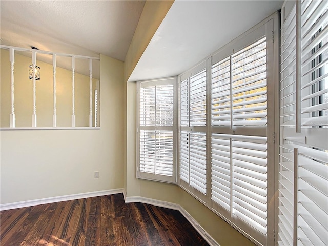 unfurnished room featuring dark wood-style floors, baseboards, and vaulted ceiling