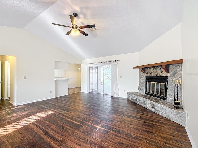 unfurnished living room with dark wood-style floors, lofted ceiling, ceiling fan, a stone fireplace, and a textured ceiling