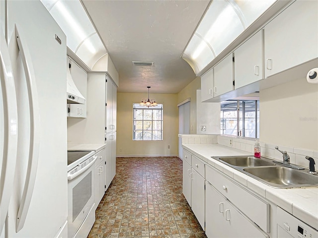 kitchen with pendant lighting, light countertops, white cabinets, a sink, and white appliances