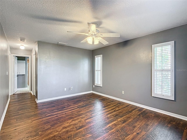 spare room with dark wood-type flooring, visible vents, ceiling fan, and baseboards