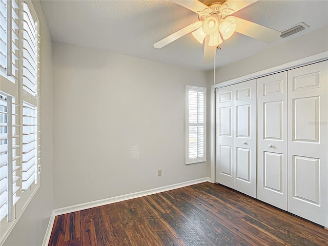 unfurnished bedroom featuring ceiling fan, visible vents, baseboards, a closet, and dark wood finished floors