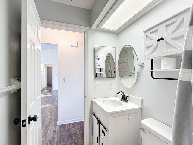 half bath with baseboards, vanity, toilet, and wood finished floors