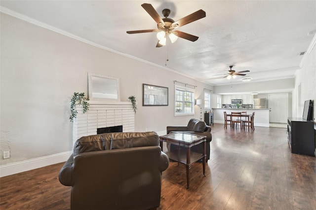 living room with a brick fireplace, crown molding, dark wood-type flooring, and ceiling fan