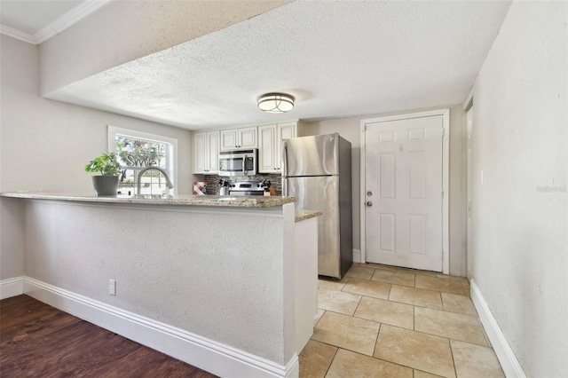 kitchen with appliances with stainless steel finishes, sink, white cabinets, kitchen peninsula, and a textured ceiling