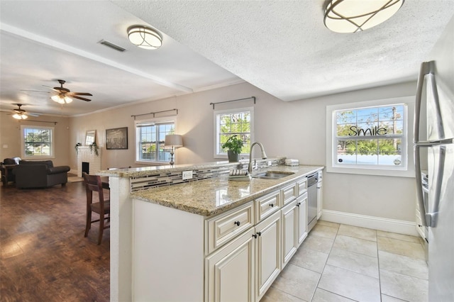 kitchen with sink, appliances with stainless steel finishes, kitchen peninsula, a fireplace, and light stone countertops