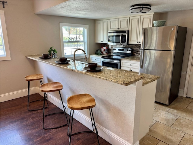 kitchen featuring stainless steel appliances, tasteful backsplash, light stone counters, a textured ceiling, and a breakfast bar area