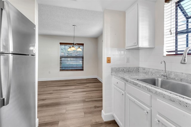 kitchen with sink, white cabinetry, decorative light fixtures, light hardwood / wood-style flooring, and stainless steel refrigerator