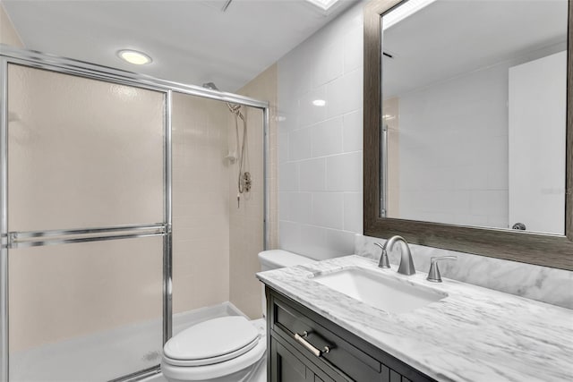 bathroom with a shower with door, vanity, tile walls, and toilet