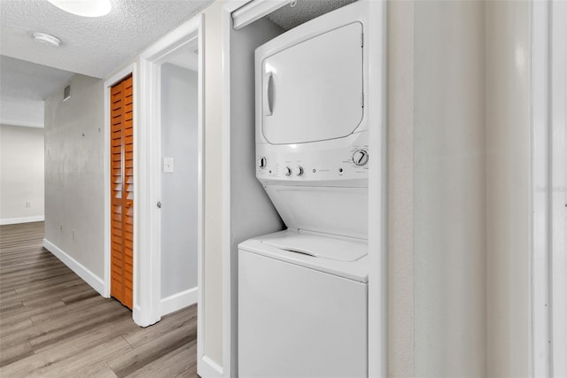 laundry area featuring stacked washer and dryer, a textured ceiling, and light wood-type flooring