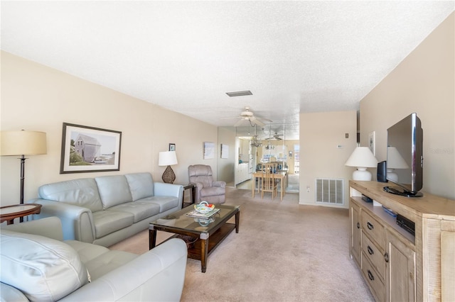 living area featuring a textured ceiling, ceiling fan, visible vents, and light colored carpet