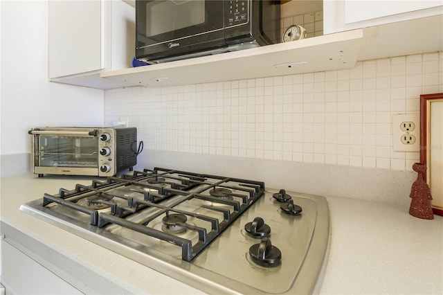 room details featuring a toaster, stainless steel gas cooktop, tasteful backsplash, white cabinetry, and black microwave