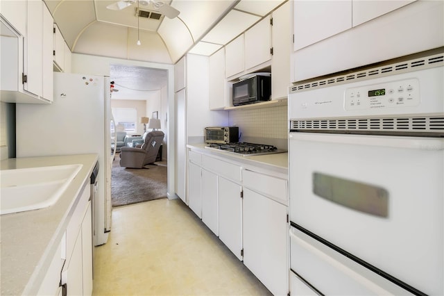 kitchen with black microwave, white cabinetry, light countertops, and white oven