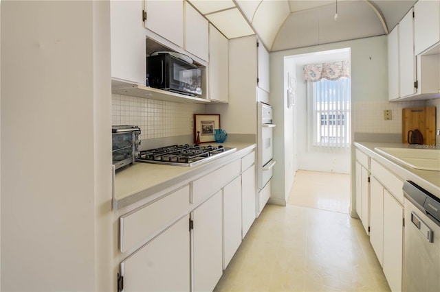 kitchen with stainless steel appliances, a sink, white cabinets, light countertops, and backsplash