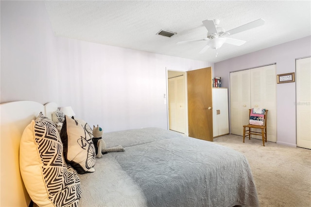 carpeted bedroom featuring a textured ceiling, ceiling fan, two closets, and visible vents