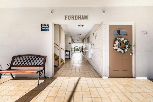 hallway featuring light tile patterned flooring, brick wall, and stairs