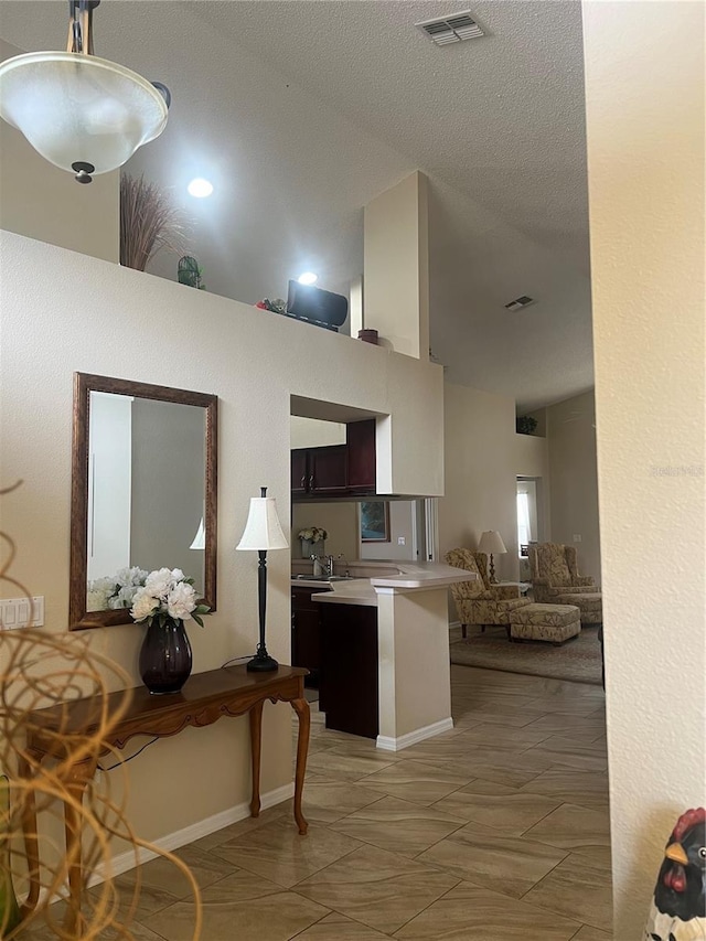 kitchen featuring sink, hanging light fixtures, high vaulted ceiling, a textured ceiling, and kitchen peninsula