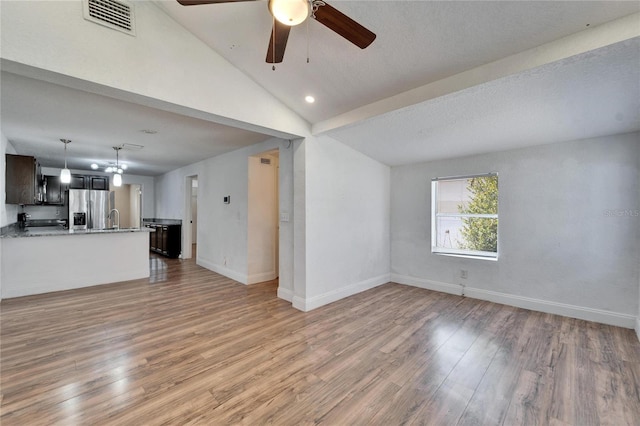 unfurnished living room with vaulted ceiling, sink, ceiling fan, a textured ceiling, and light hardwood / wood-style flooring