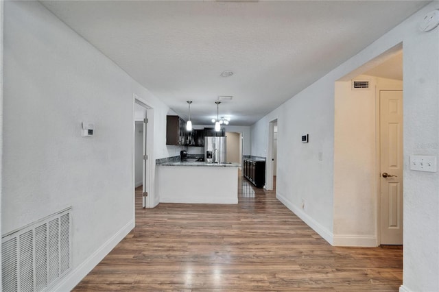 kitchen featuring stainless steel refrigerator with ice dispenser, hanging light fixtures, a textured ceiling, dark hardwood / wood-style floors, and kitchen peninsula