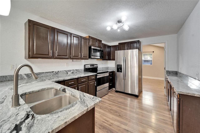 kitchen featuring stainless steel appliances, dark brown cabinets, sink, and light stone counters