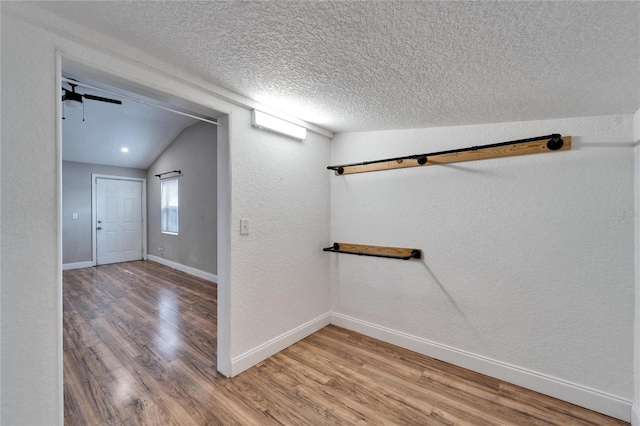 hallway with vaulted ceiling, hardwood / wood-style floors, and a textured ceiling