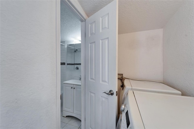 bathroom featuring vanity, tiled shower, independent washer and dryer, tile patterned floors, and a textured ceiling