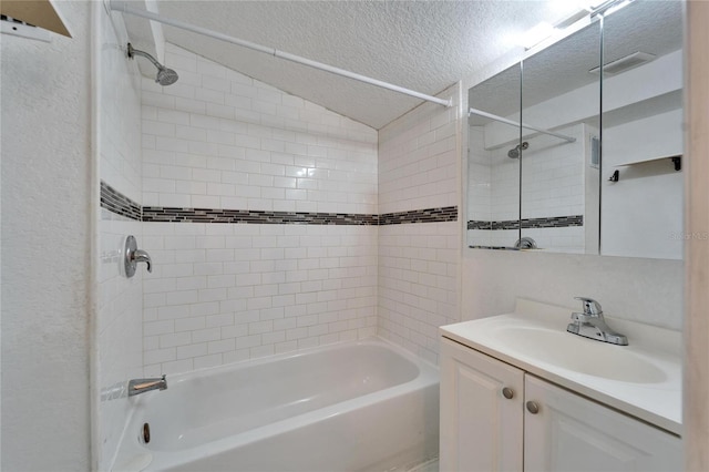 bathroom featuring vanity, tiled shower / bath combo, vaulted ceiling, and a textured ceiling